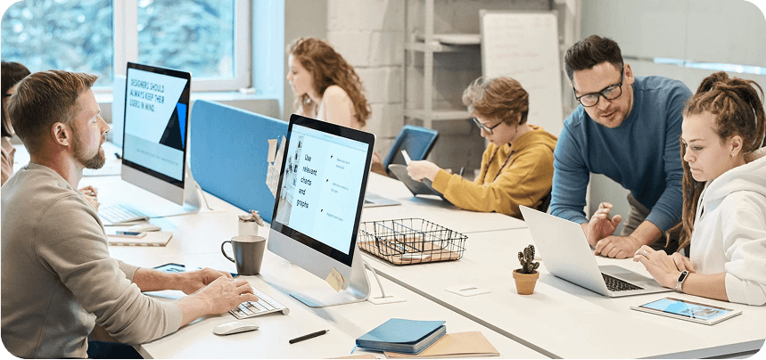 Design or creative team collaborating in a bright, modern office, focused on tasks using laptops and desktop monitors.